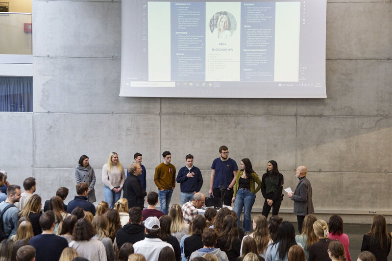 Ein Vortrag wurde vor Publikum mit mehreren Personen und einer großen Präsentationsleinwand im Hintergrund gehalten.