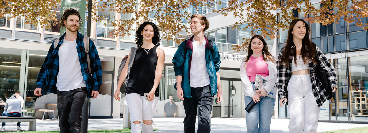Fünf Studierende gehen gemeinsam über den Campus bei Frühlingswetter