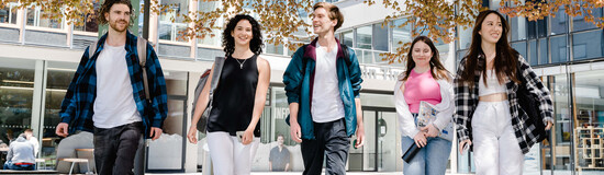 Fünf Studierende gehen gemeinsam über den Campus bei Frühlingswetter