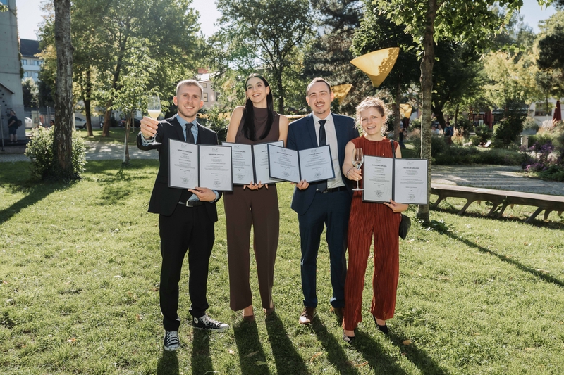 Gruppe von Absolvent:innen bei der Sponsion der HOK, lachend und mit Sponsionsmappen im Park.