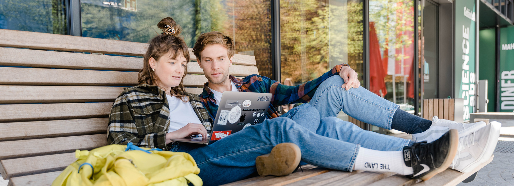 Zwei Studierende arbeiten gemeinsam am Laptop auf einer Bank vor der HOK
