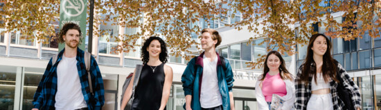 Fünf Studierende gehen gemeinsam über den Campus bei Frühlingswetter
