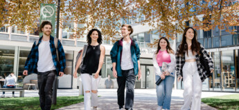Fünf Studierende gehen gemeinsam über den Campus bei Frühlingswetter