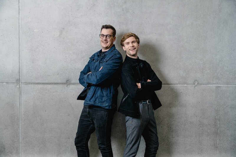 Zwei Studierende der HOK stehen entspannt vor einer Betonwand und blicken in die Kamera.