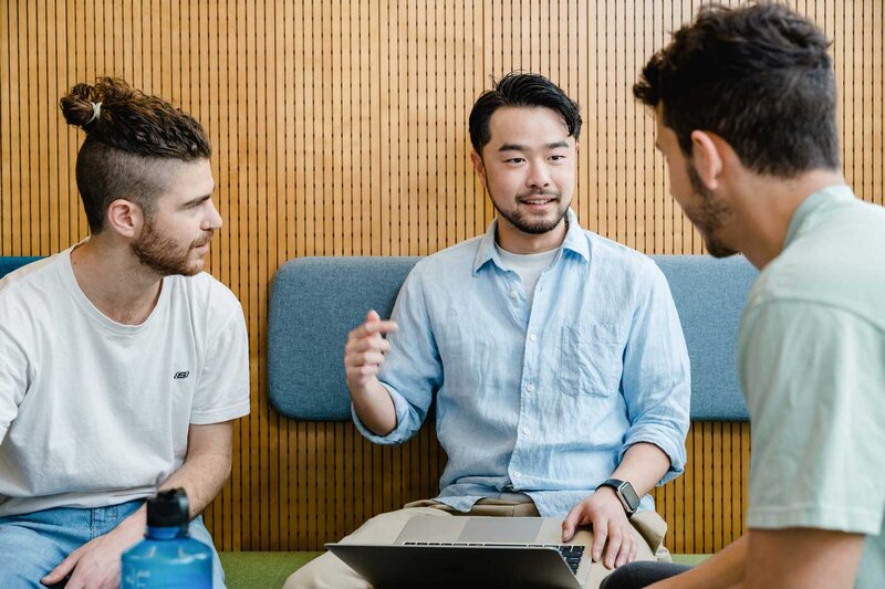 Drei Studierende im Gespräch bei Gruppenarbeit mit Laptop in moderner Sitzecke