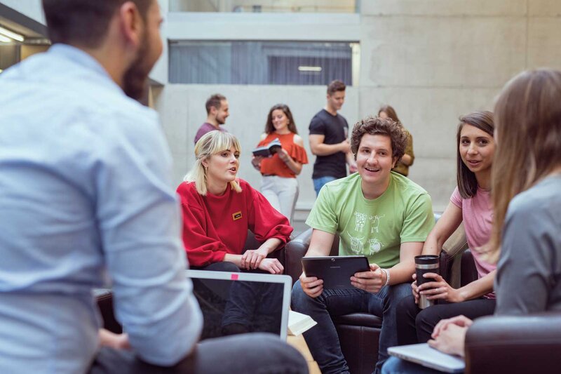 Gruppe von Studierenden der HOK arbeitet in der Aula gemeinsam an einem Projekt und diskutiert Ideen.