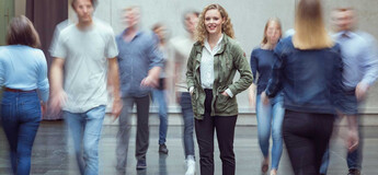 Viele Personen bewegen sich durch die Aula der HOK, und im Zentrum des Bildes steht eine Frau und blickt in die Kamera.