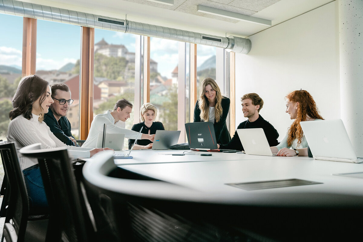 Studierendengruppe arbeitet gemeinsam mit Laptops in hellem Seminarraum mit Alpenblick