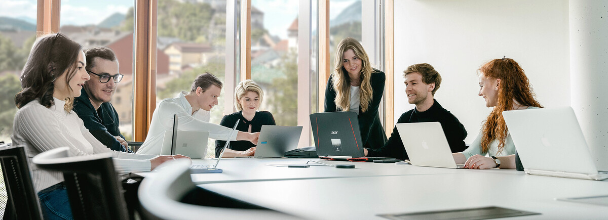 Studierendengruppe arbeitet gemeinsam mit Laptops in hellem Seminarraum mit Alpenblick