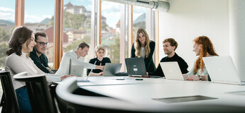 Studierendengruppe arbeitet gemeinsam mit Laptops in hellem Seminarraum mit Alpenblick
