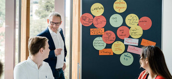 Dozent der HOK erläutert Studierenden Seminarinhalte an einer Pinnwand mit Notizen