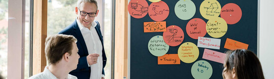 Dozent der HOK erläutert Studierenden Seminarinhalte an einer Pinnwand mit Notizen
