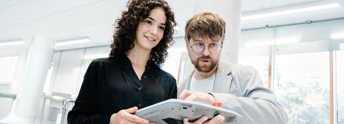 Zwei Personen steuern eine industrielle Automatisierungsanlage über ein Tablet im Labor.