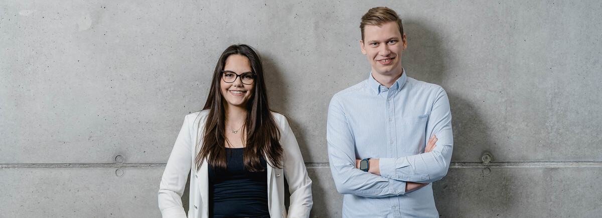 Zwei Studierende der HOK vor einer Betonwand – Portrait im modernen Campusstil.