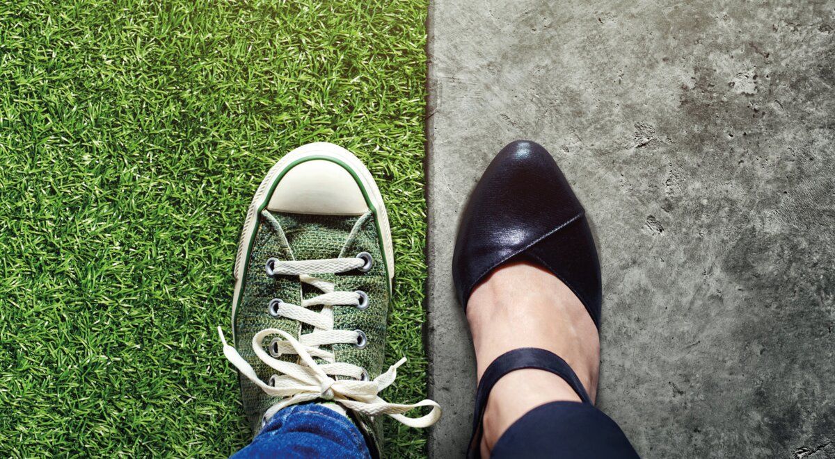 Ein Sneaker auf Gras und ein Business-Schuh auf Beton nebeneinander.