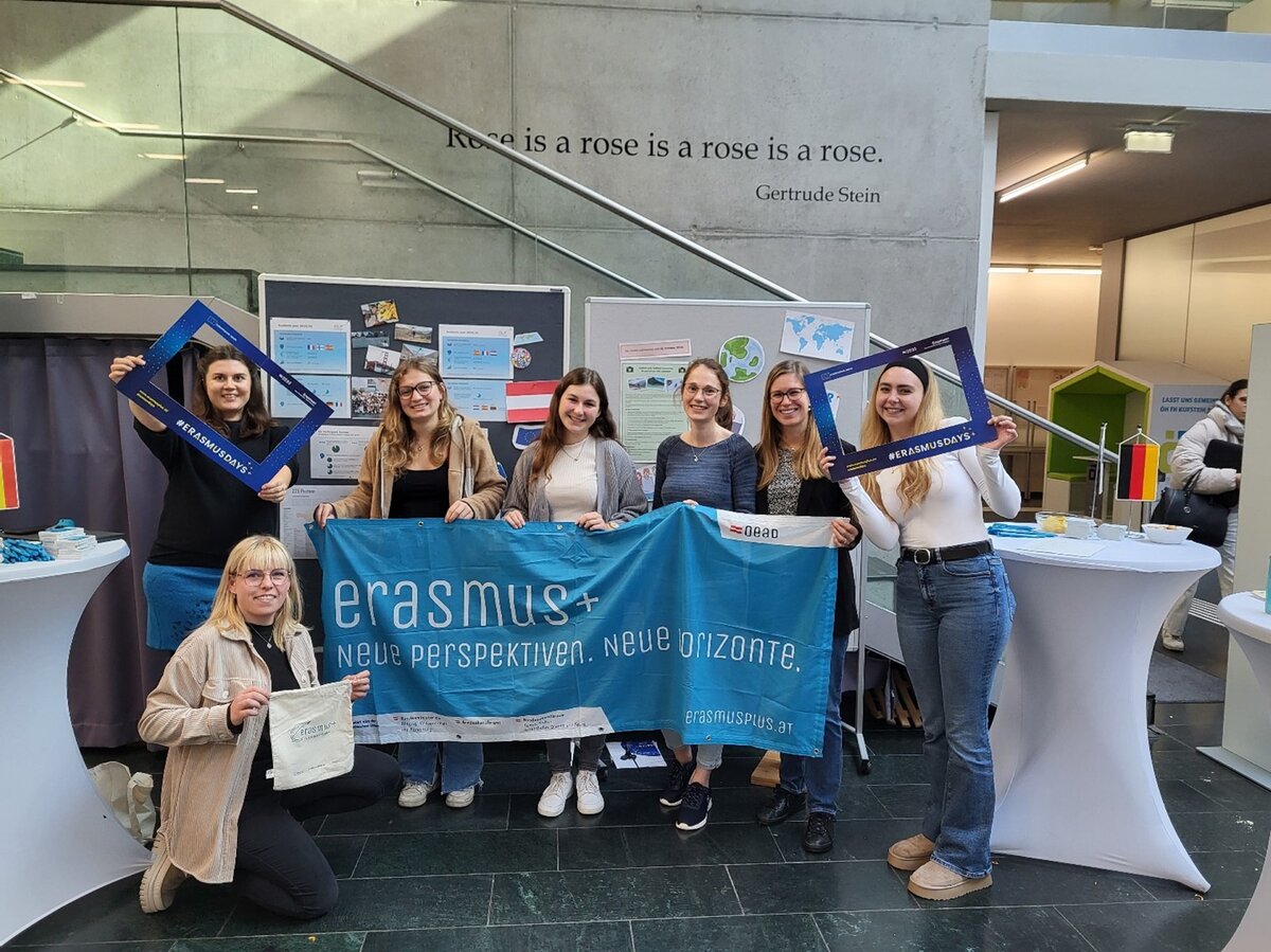 Mitarbeiterinnen mit zwei Besucherinnen in der Aula während der Erasmus Ausstellung