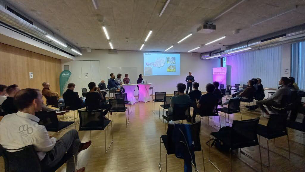 Personen siitzen auf Stühlen und schauen auf eine Projektion an der Wand.