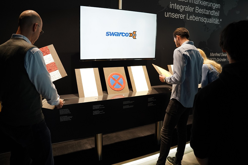 Student steht for einem Ausstellungstisch mit Bildschirmscreen Swarco