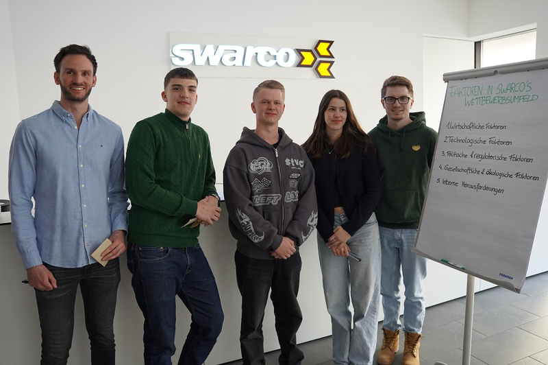 Studierende stehen in Reihe vor Flipchart