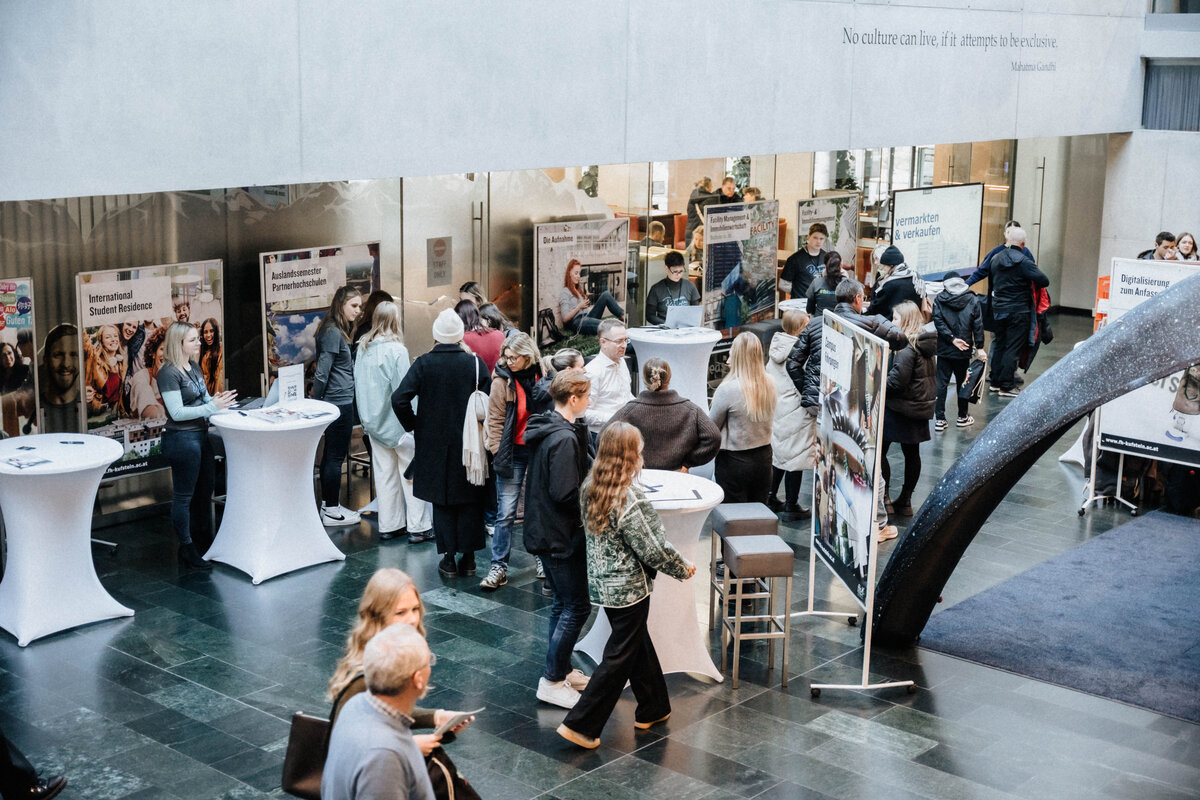 Blick von oben auf die Aula während eines Open House an der HOK mit Infoständen und Besucher:innen.