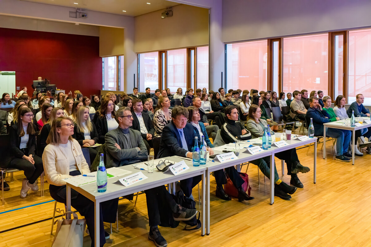 Ein Blick ins Publikum des Festsaals der HOK: In der ersten Reihe sitzen die Juror:innen des 7€ Cash@School-Wettbewerbs, dahinter die Schüler:innen.