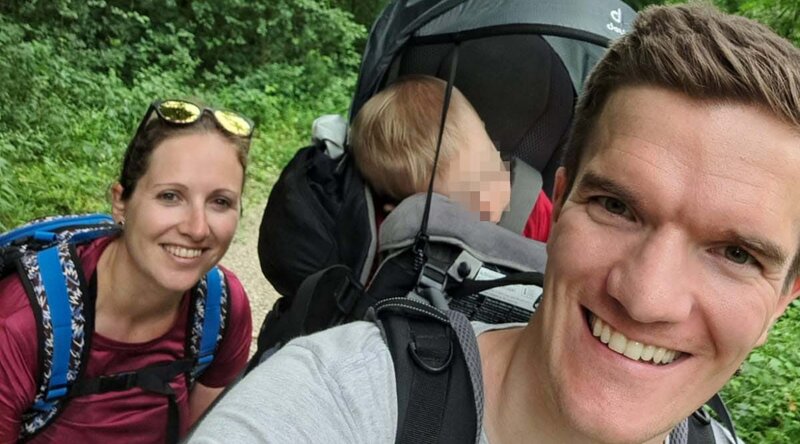 Teresa und Peter beim Wandern mit ihrem Kind in einer Rückentrage auf einem Waldweg.