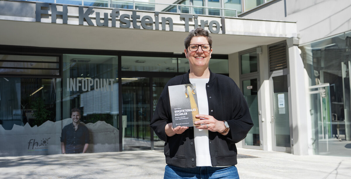 Prof. (FH) PD Dr. Agnes Bidmon vor dem Eingang der FH mit Buch in der Hand