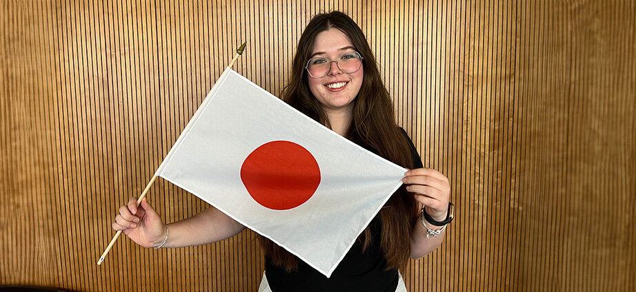 Studentin steht vor einer Holzwand mit einer Japan-Flagge