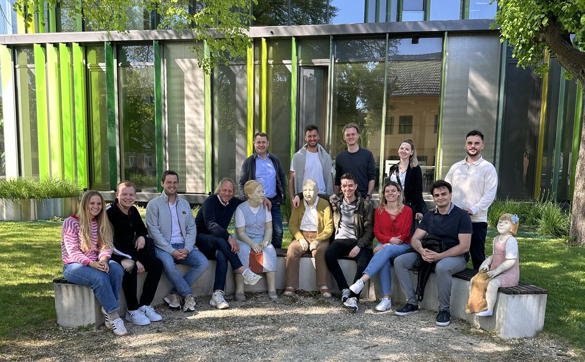 Eine Gruppe von Personen sitzt draußen in einem Halbkreis auf einer Betonmauer.