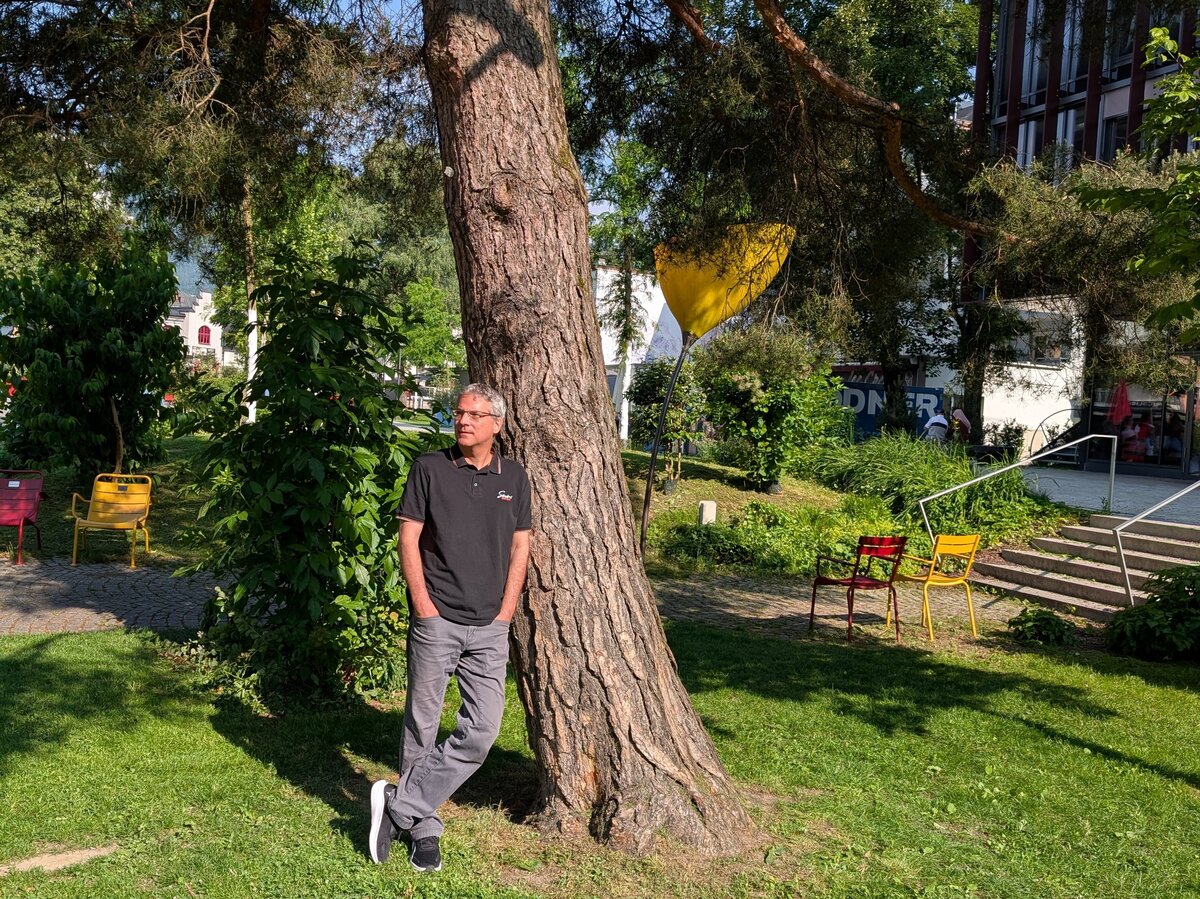 Ein Mann in Jeans und T-Shirt lehnt an einem Baum im Park.