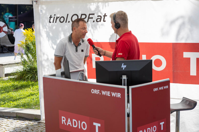 ORF-Moderator im roten Poloshirt interviewt Thomas Madritsch, Geschäftsführer der HOK, bei der Sommerfrische 2025 am Radiostand.