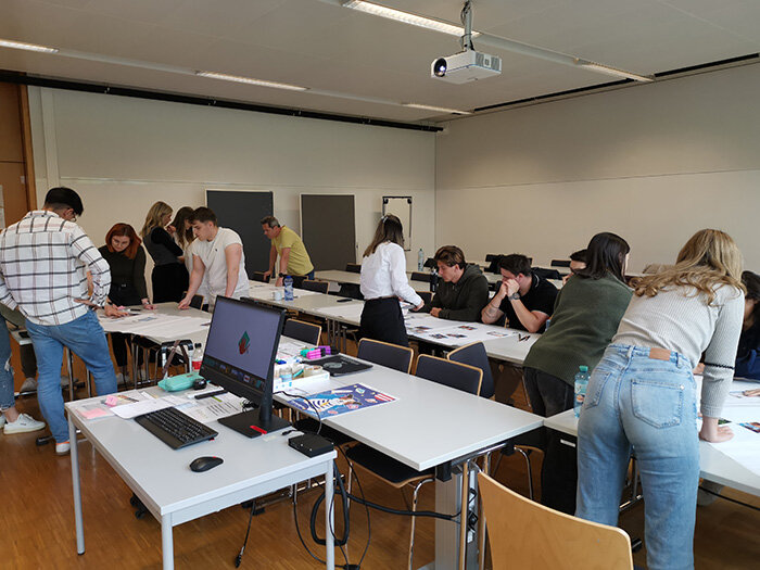 Studierende arbeiten in Gruppen während eines Climate-Fresk-Workshops an Tischen mit Materialien und Karten.