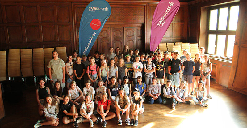 Teilnehmende stehen für ein Gruppenfoto in einem alten holzverkleideten Raum zusammen.