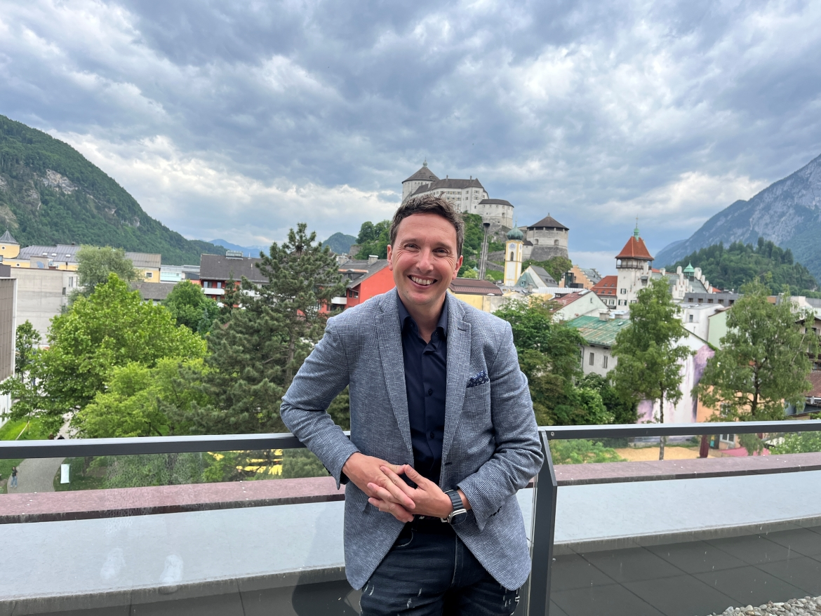 Mann in grauem Sakko steht lächelnd auf einer Terrasse im Hintergrund die Festung Kufstein und die umliegende Altstadt