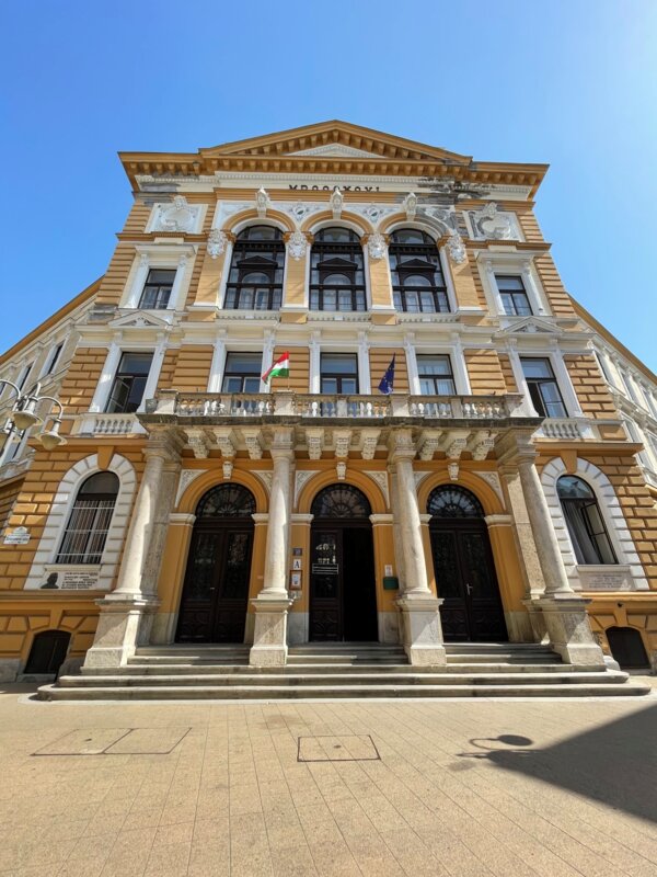 Historisches Universitätsgebäude in Budapest mit ungarischer und EU-Flagge an der Fassade, aufgenommen bei Sonnenschein