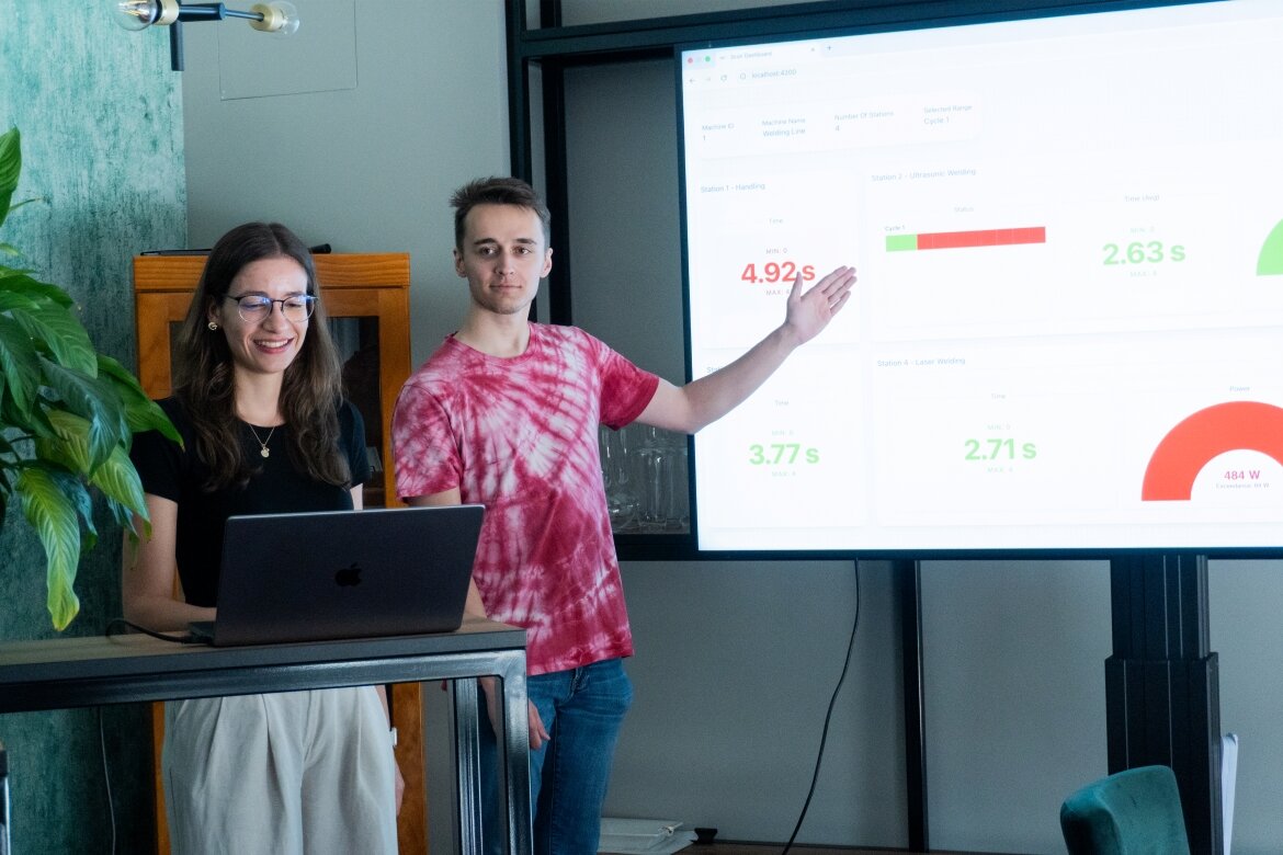 Zwei Studierende aus dem Praxisprojekt der HOK bei ihrer Abschlusspräsentation im Hause der Firma 3CON mit den visualisierten Sensordaten, abgebildet auf einem Bildschirm. 