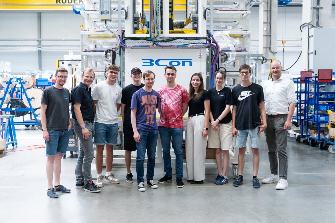Praxisprojekt der HOK: Das Studierendenteam gemeinsam mit Vertreter und Ansprechpartner vor einer automatisierten Fertigungsanlage des Partnerunternehmens 3CON