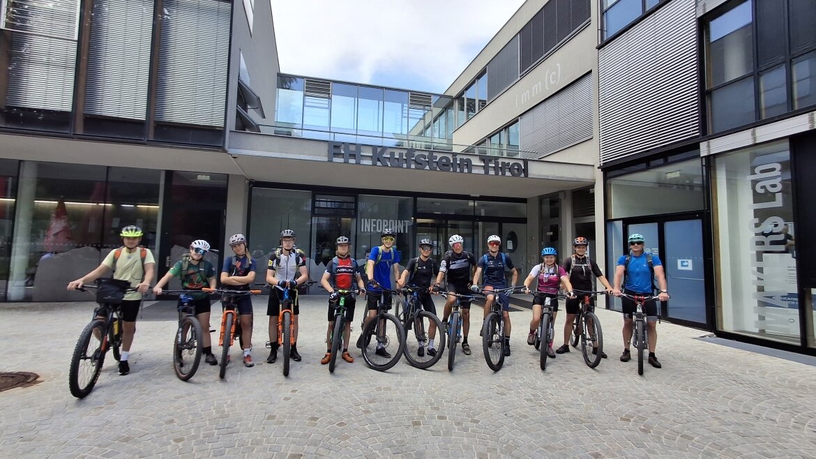 Eine Gruppe von Schülerinnen und Schülern mit Mountainbikes steht vor dem Eingangsbereich der HOK, bereit für eine gemeinsame Ausfahrt.