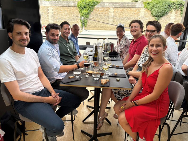 Teilnehmende der AIEST-Jahrestagung 2025 sitzen fröhlich an einem langen Tisch bei einem Abendessen. Wein, Wasser und kleine Snacks stehen auf dem Tisch, alle wirken entspannt und gut gelaunt.