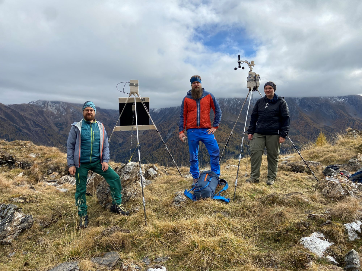 Drei Personen stehen mit zwei Anlagen auf dem Berg nebeneinander.