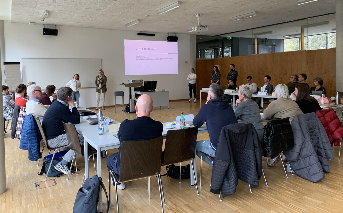 Eine Gruppe von Menschen von Hinten in einem Hörsaal, vorne eine Präsentation.