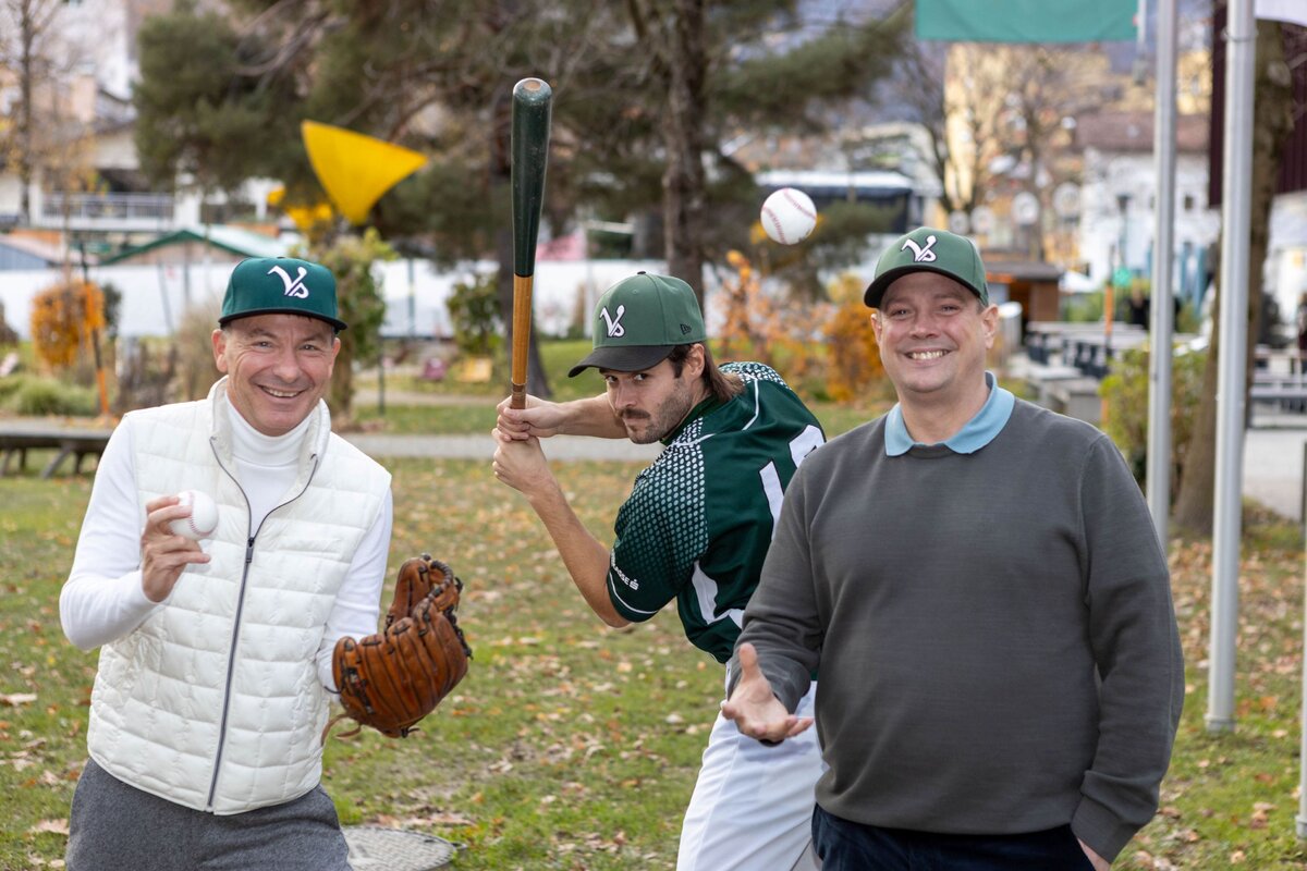 Drei Personen stehen nebeneinander mit jeweils einem Baseballhandschuh, -schläger und -ball