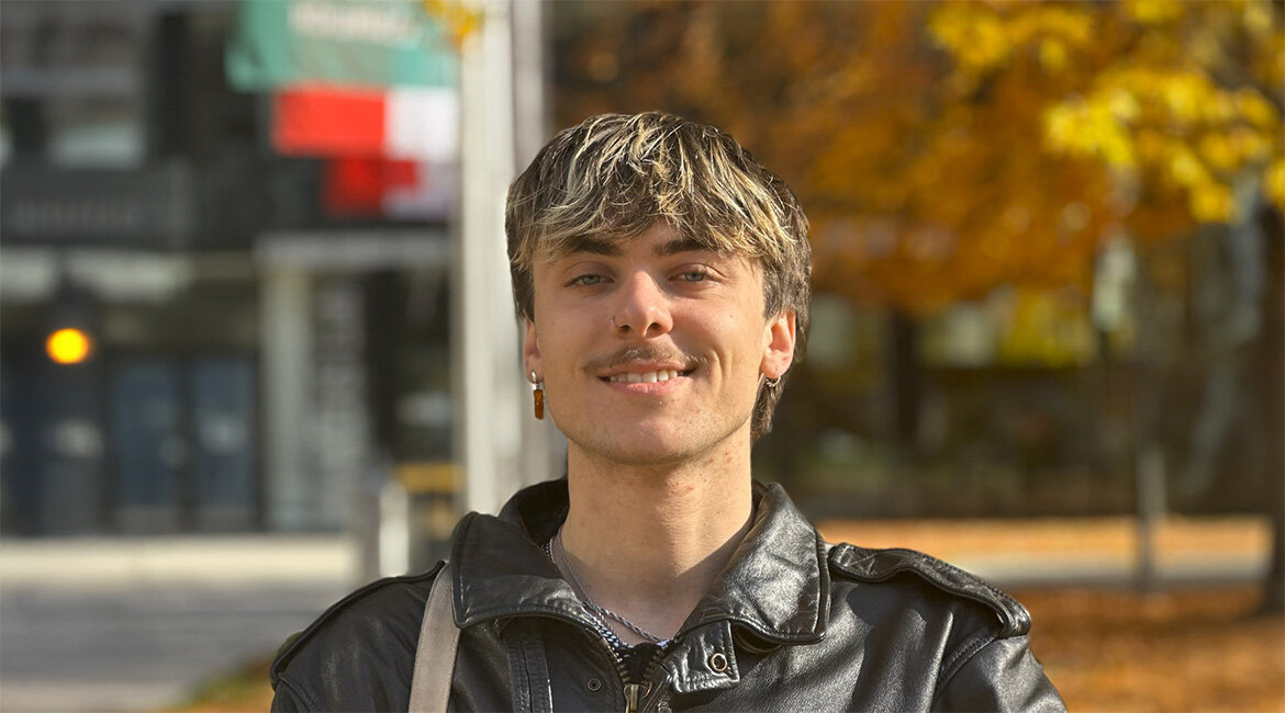 Person steht im Freien vor einem Gebäude und einem Baum.