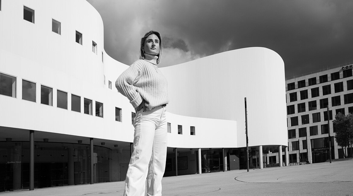 Schwarz-Weiß-Foto von Melina Münstermann, die vor einem Gebäude steht.