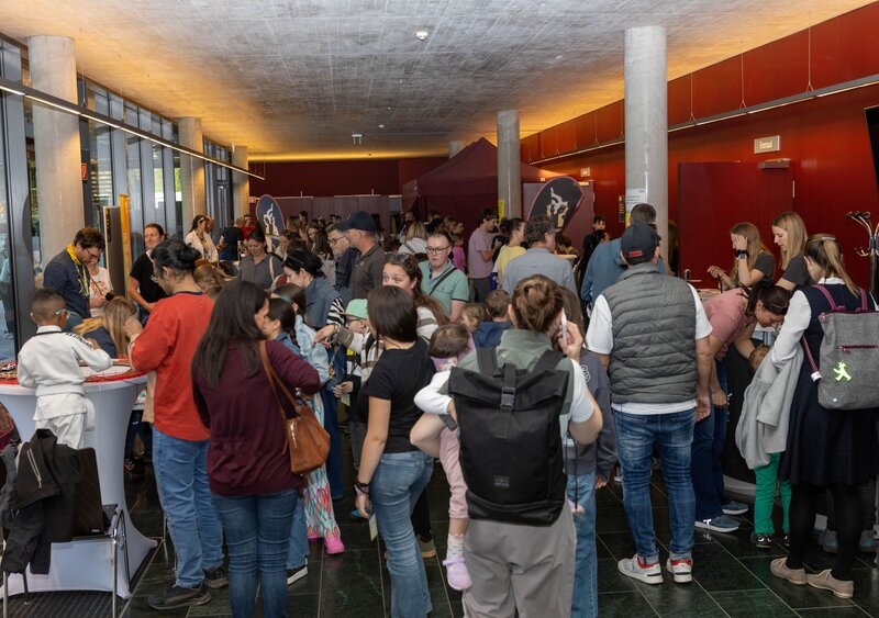 Besucherinnen bewegen sich durch das Foyer der Kufsteiner Hochschule und entdecken die vielfältigen Mitmach-Stationen der Langen Nacht der Forschung 