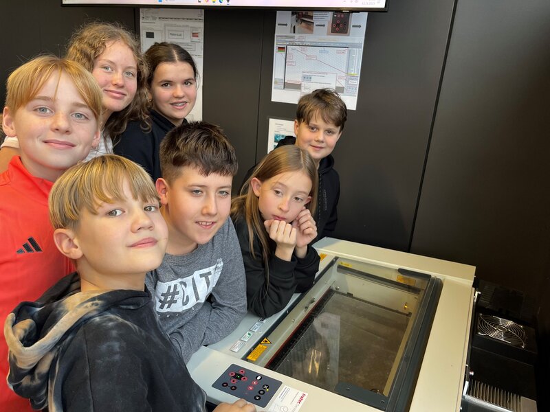 Schüler:innen stehen am Lasercutter und beobachten das Geschehen.