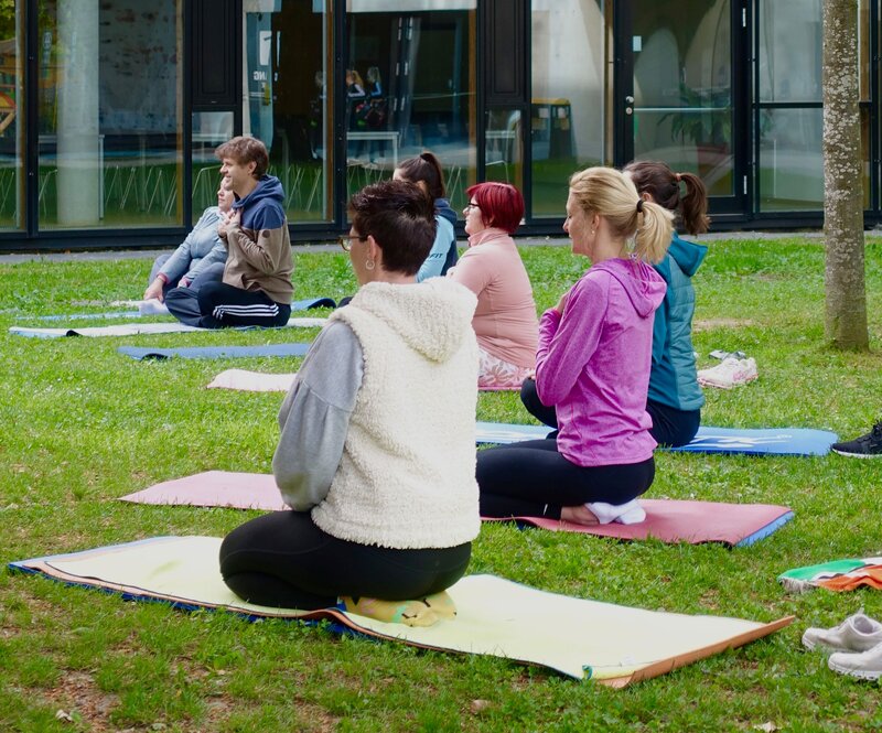 Personen sitzen im Stadtpark vor dem Gebäude der HOK auf einer Yogamatte.
