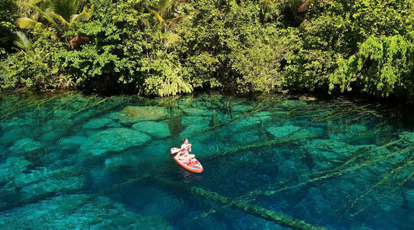 Eine Person mit Boot in einer klaren, tropischen Lagune in Indonesien umgeben von Felsen und Natur. | © privat