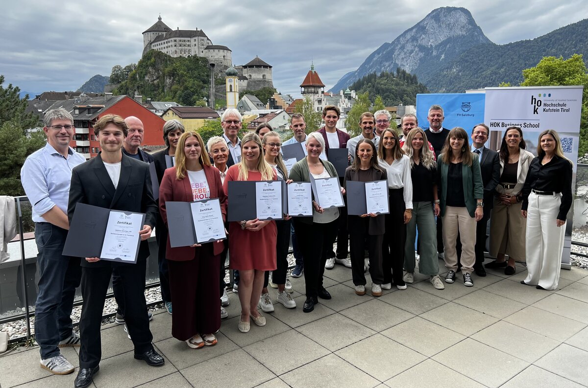 Absolvierende präsentieren stolz ihre Zertifikate bei der Feier auf der Dachterrasse der HOK | Hochschule Kufstein Tirol.