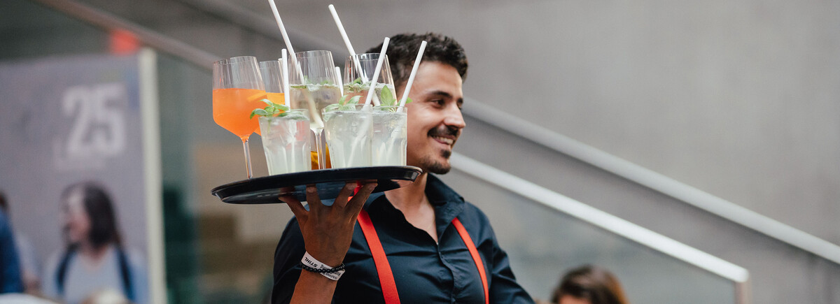 Servicekraft mit Tablett voller Cocktails bei Veranstaltung an der HOK.